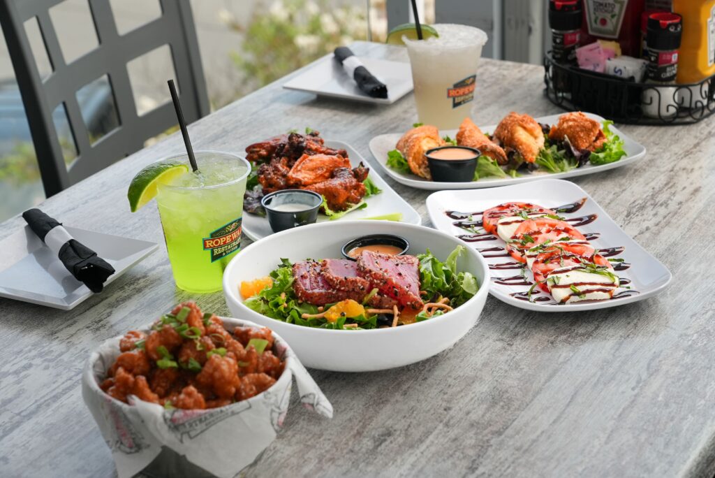 A variety of dishes on a table with two cocktails.