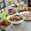 A variety of dishes on a table with two cocktails.